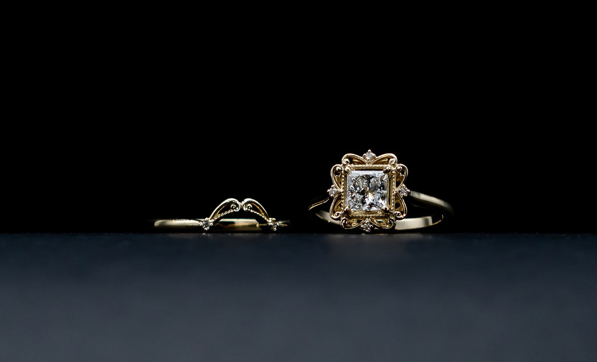Two gold rings on a dark background, one with a square diamond setting.