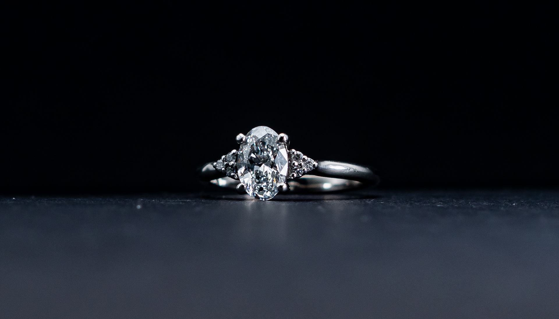 Diamond engagement ring on a dark reflective surface against a black background