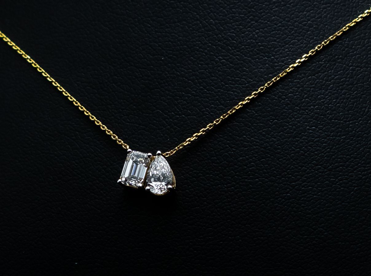 Gold chain necklace with a small silver pendant on a black background