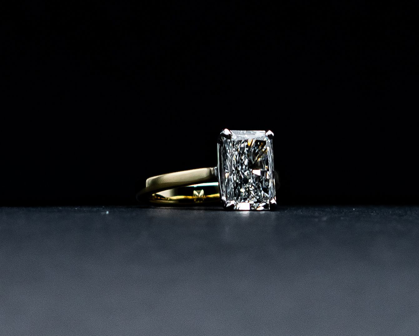 Diamond ring with a rectangular clear gemstone on a dark surface against a black background