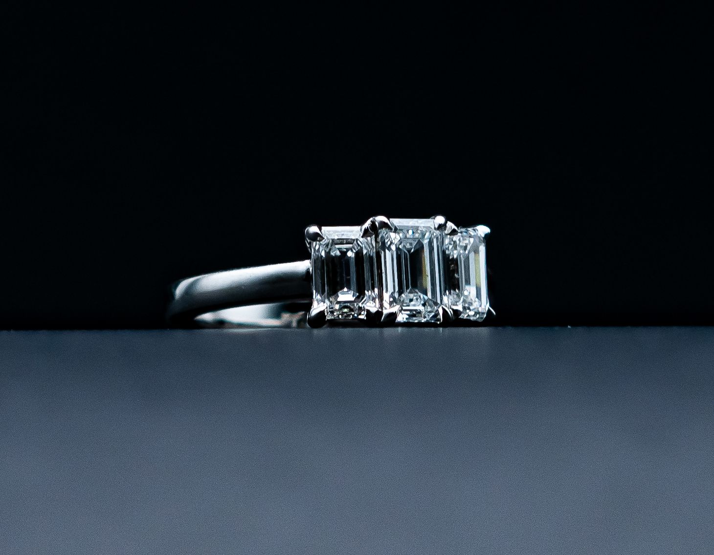 Three-stone diamond ring on a dark surface against a black background