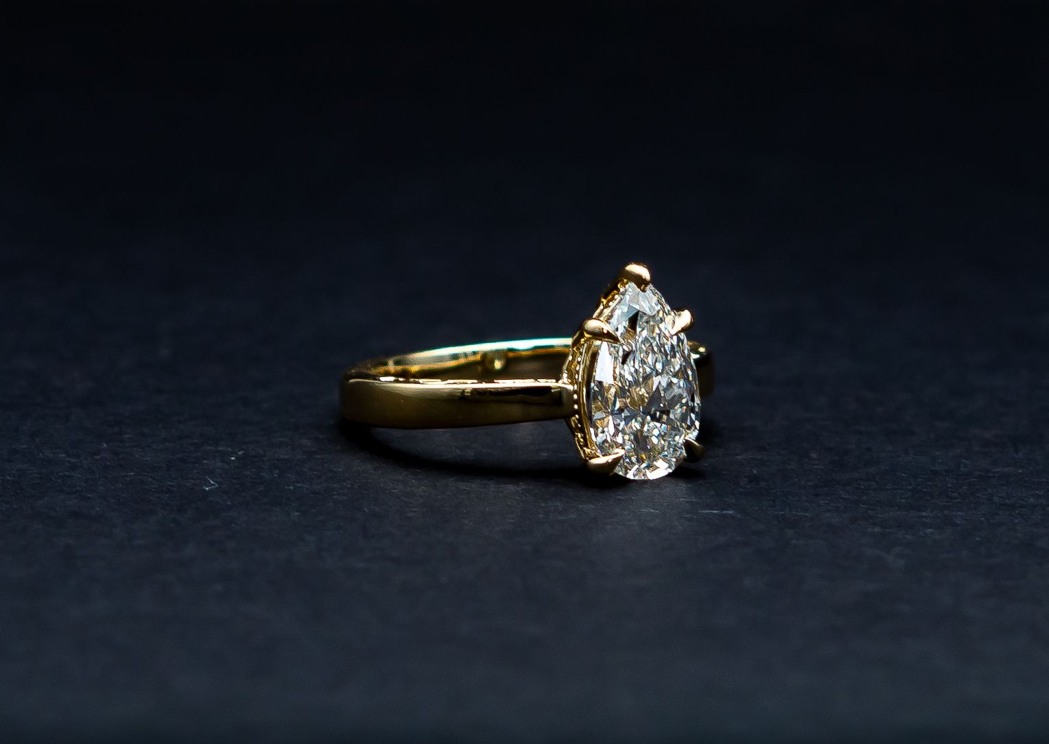 Gold ring with a teardrop-shaped diamond on a dark background