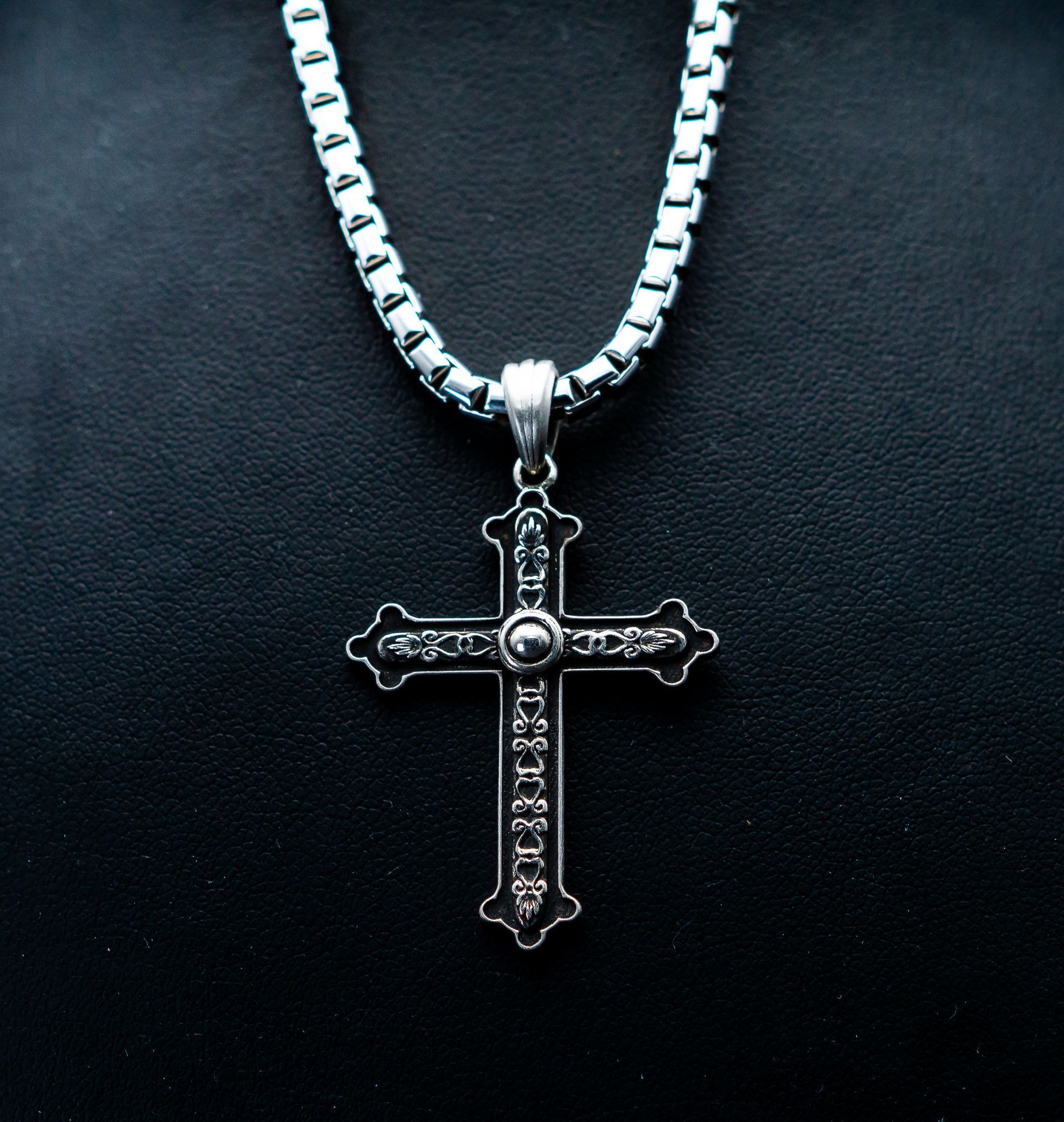 Silver cross pendant on a chain against a black background