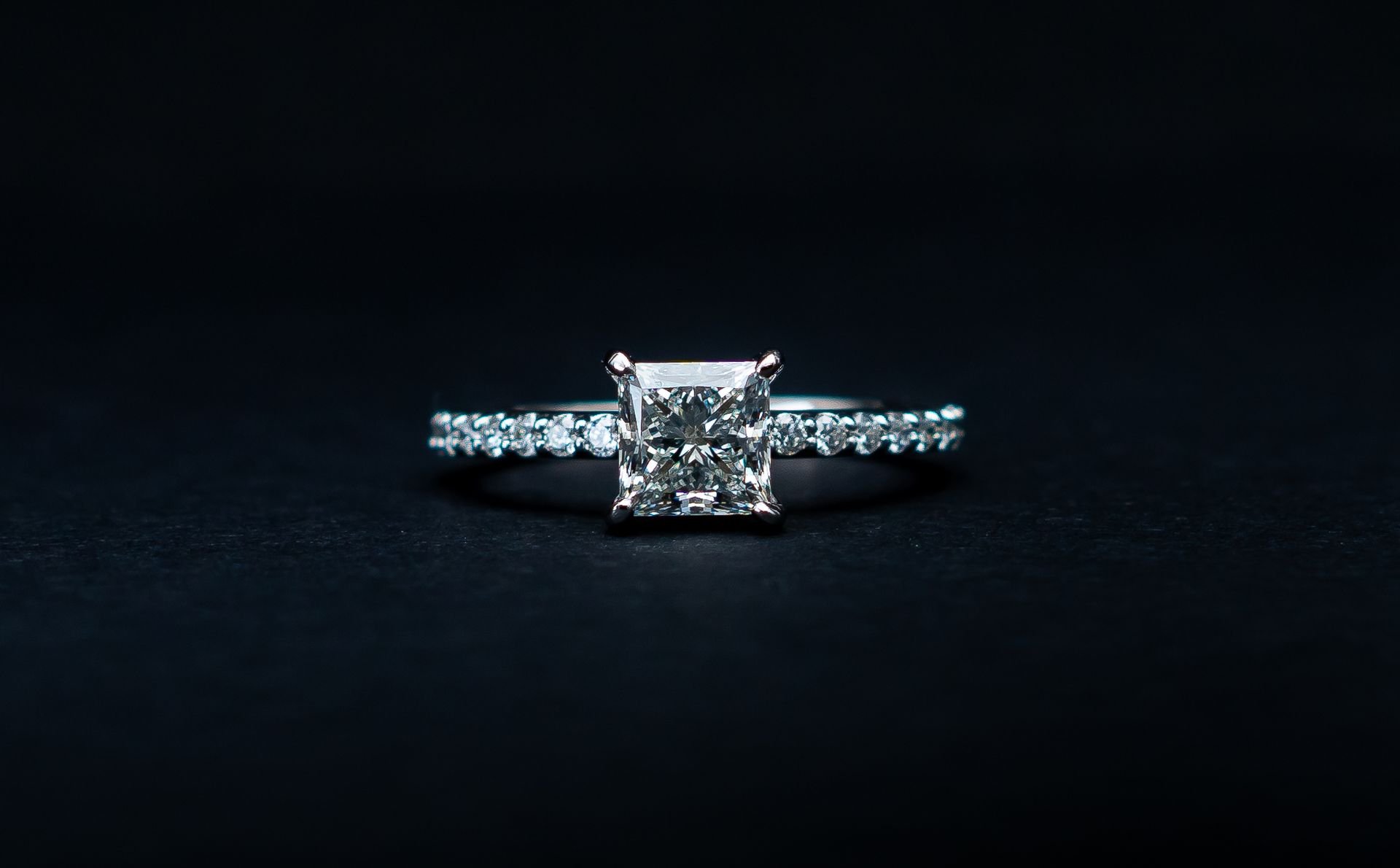 Diamond engagement ring with a square center stone on a dark background