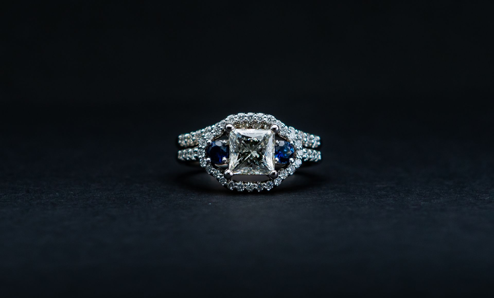 Silver ring with a square clear gemstone and blue accents on a dark background