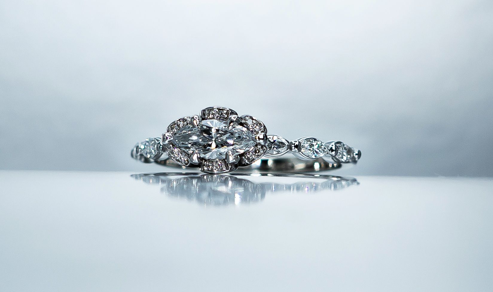 Silver jeweled ring on a glossy white surface with a soft gray background