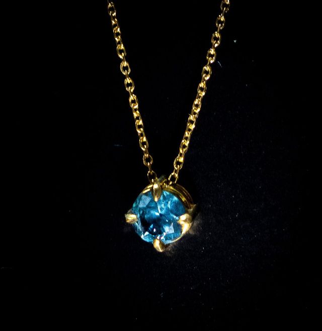 Gold necklace with a round blue gemstone pendant on a black background