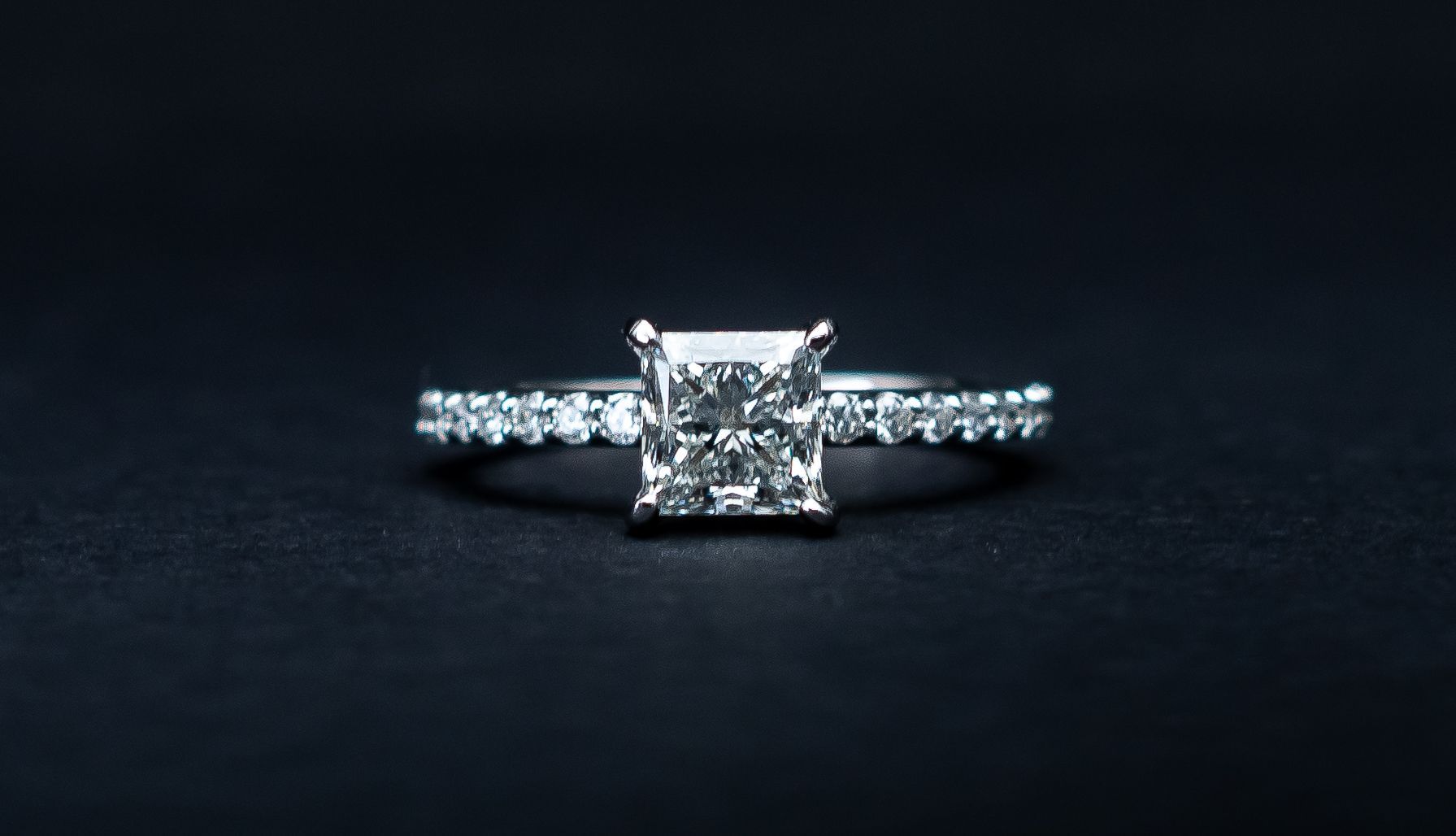 Diamond engagement ring with a square-cut center stone on a dark background