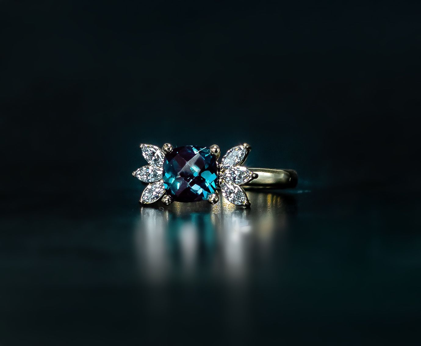 Diamond ring with blue center stone and side diamonds on a dark reflective surface