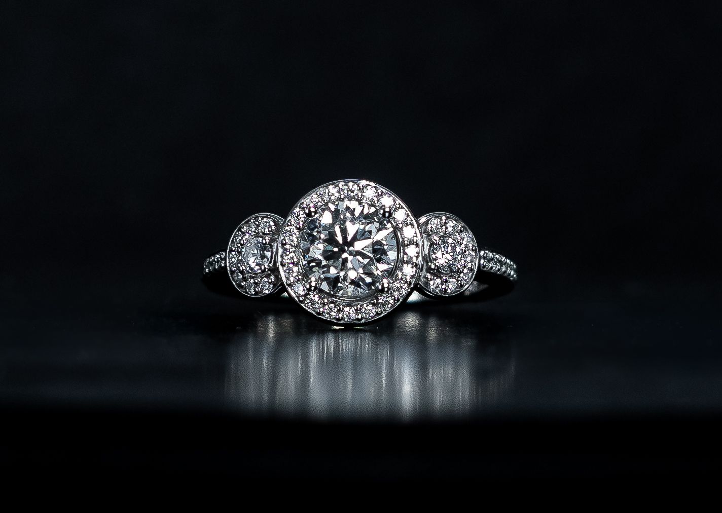 Diamond engagement ring with round center stone and side stones on a black background
