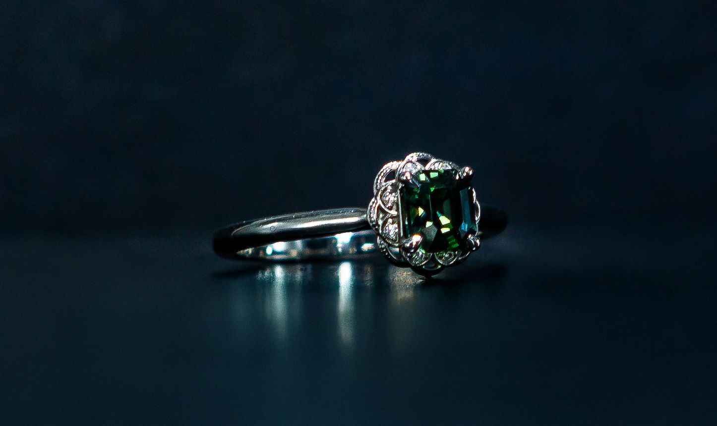 A silver ring with a dark green gemstone on a dark background.