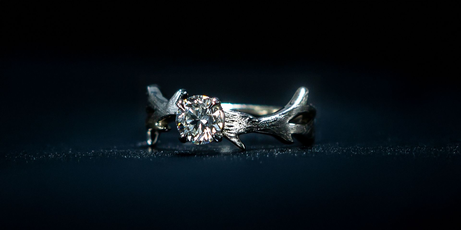 Silver diamond ring on a dark blue background, lit with a soft sparkle