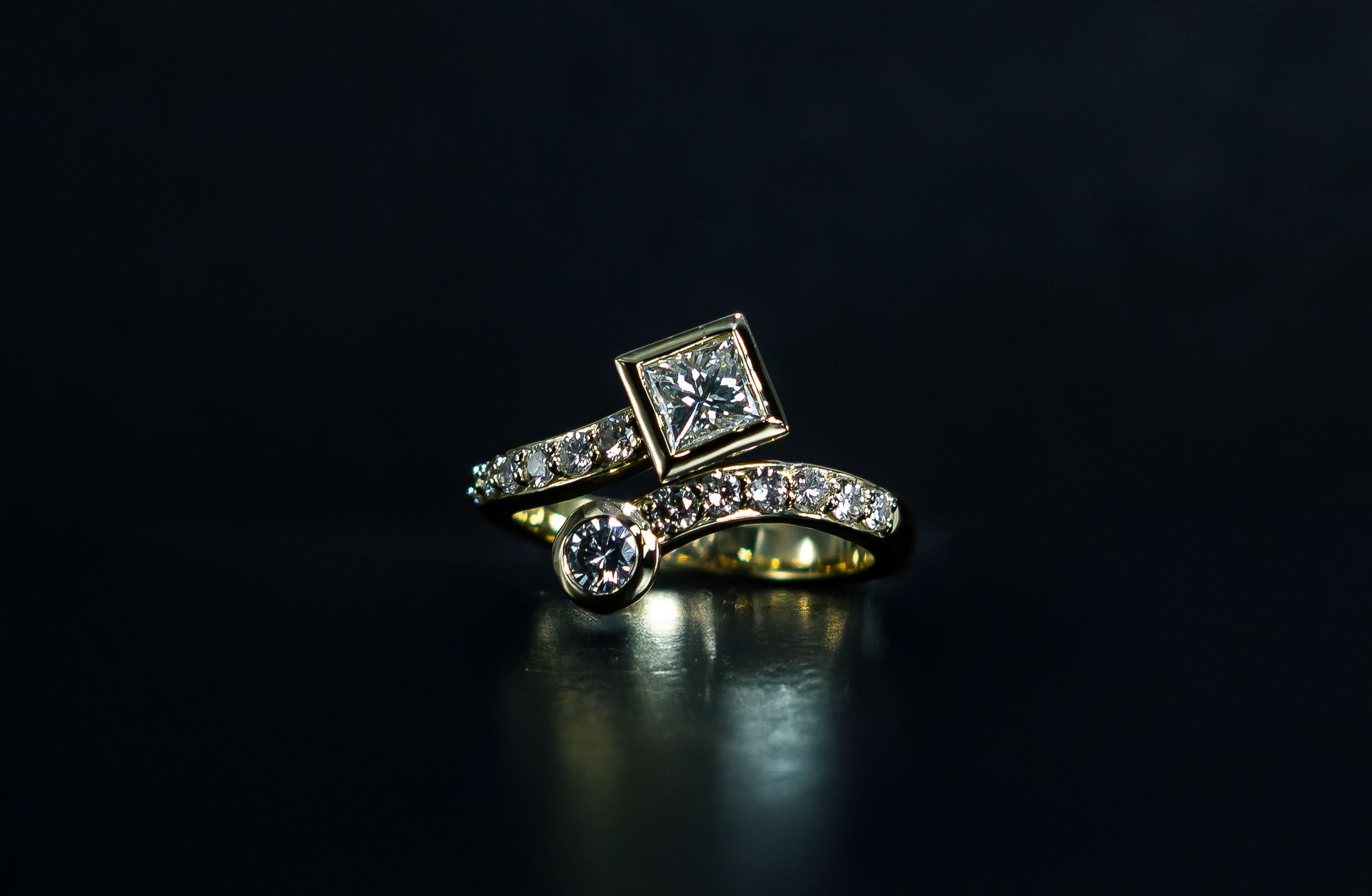 Two diamond rings on a dark background, one square-cut and one round-cut, with a gold band