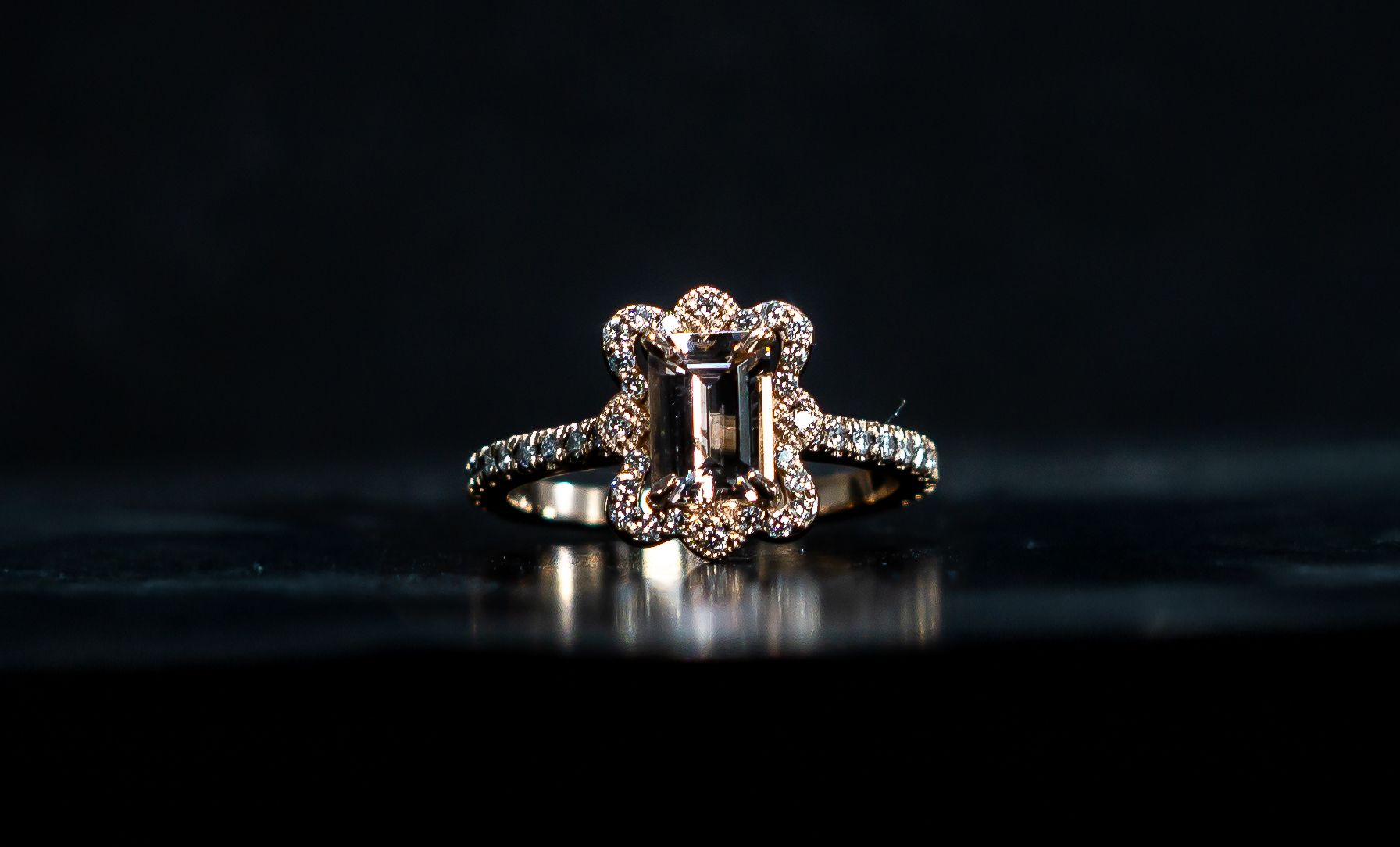 Silver ring with a central gemstone and small side stones on a dark reflective surface