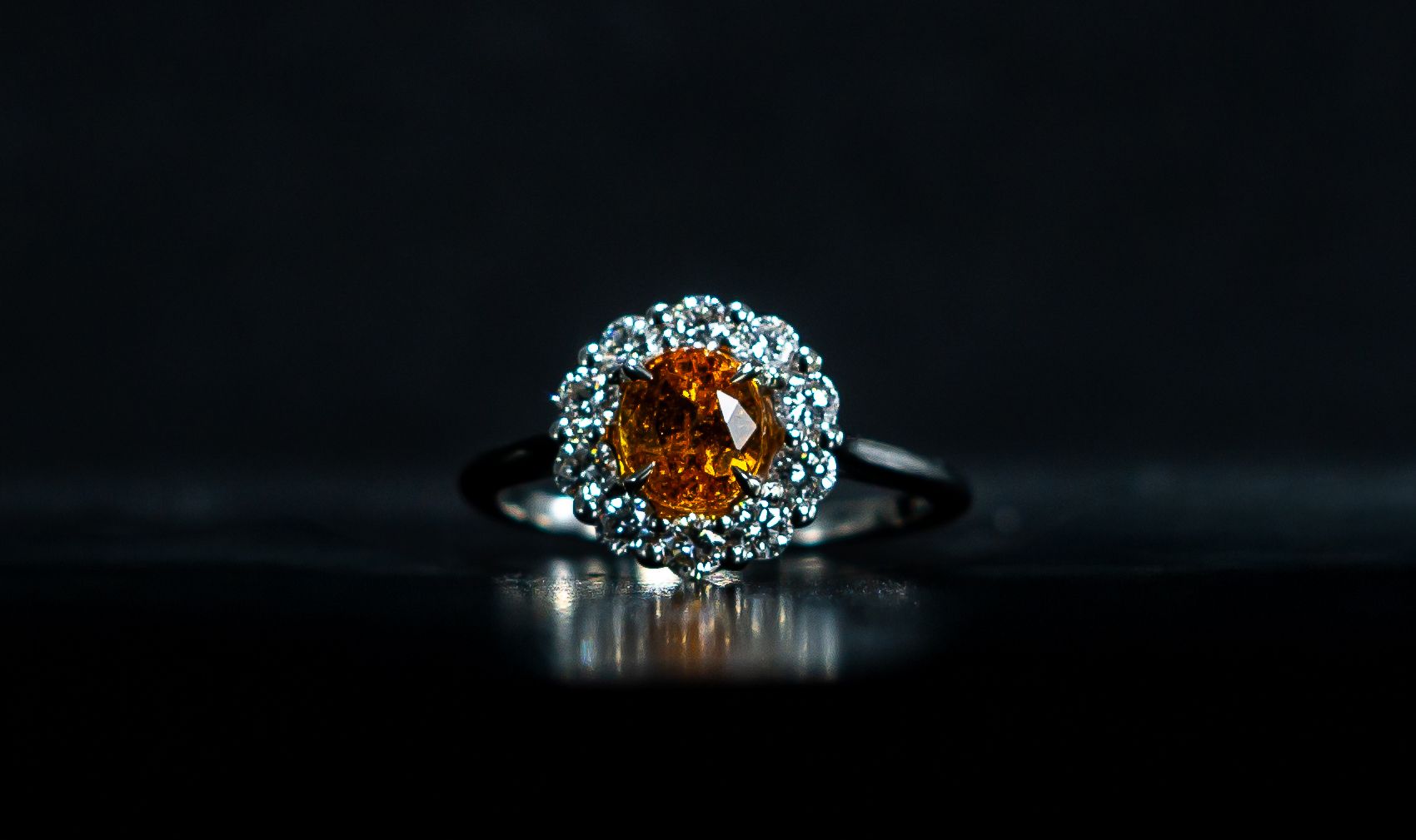 Diamond ring with an amber center stone on a dark reflective surface