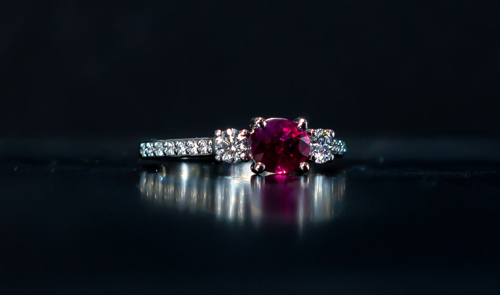 Diamond ring with a large red gemstone on a dark reflective surface