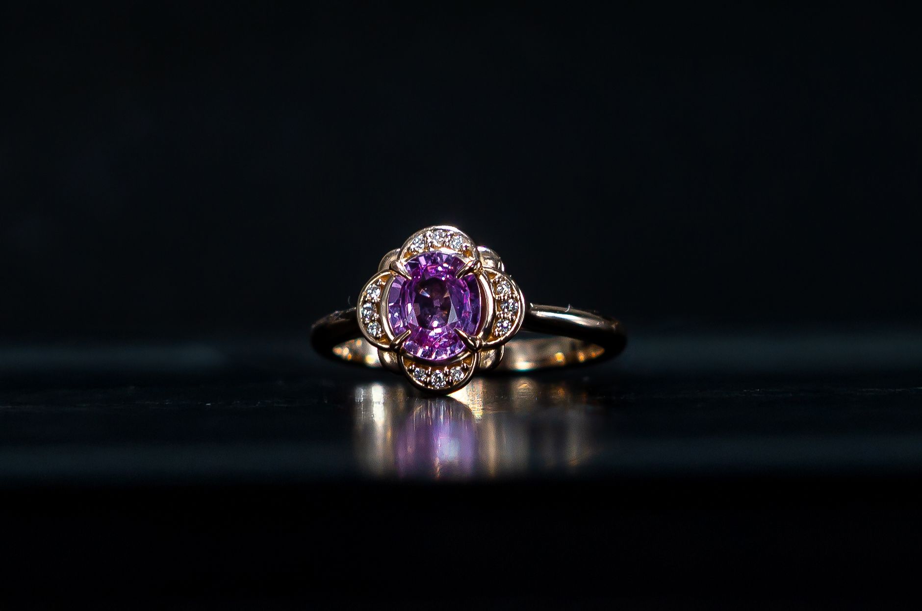 Gold ring with a purple gemstone and halo setting on a dark reflective surface