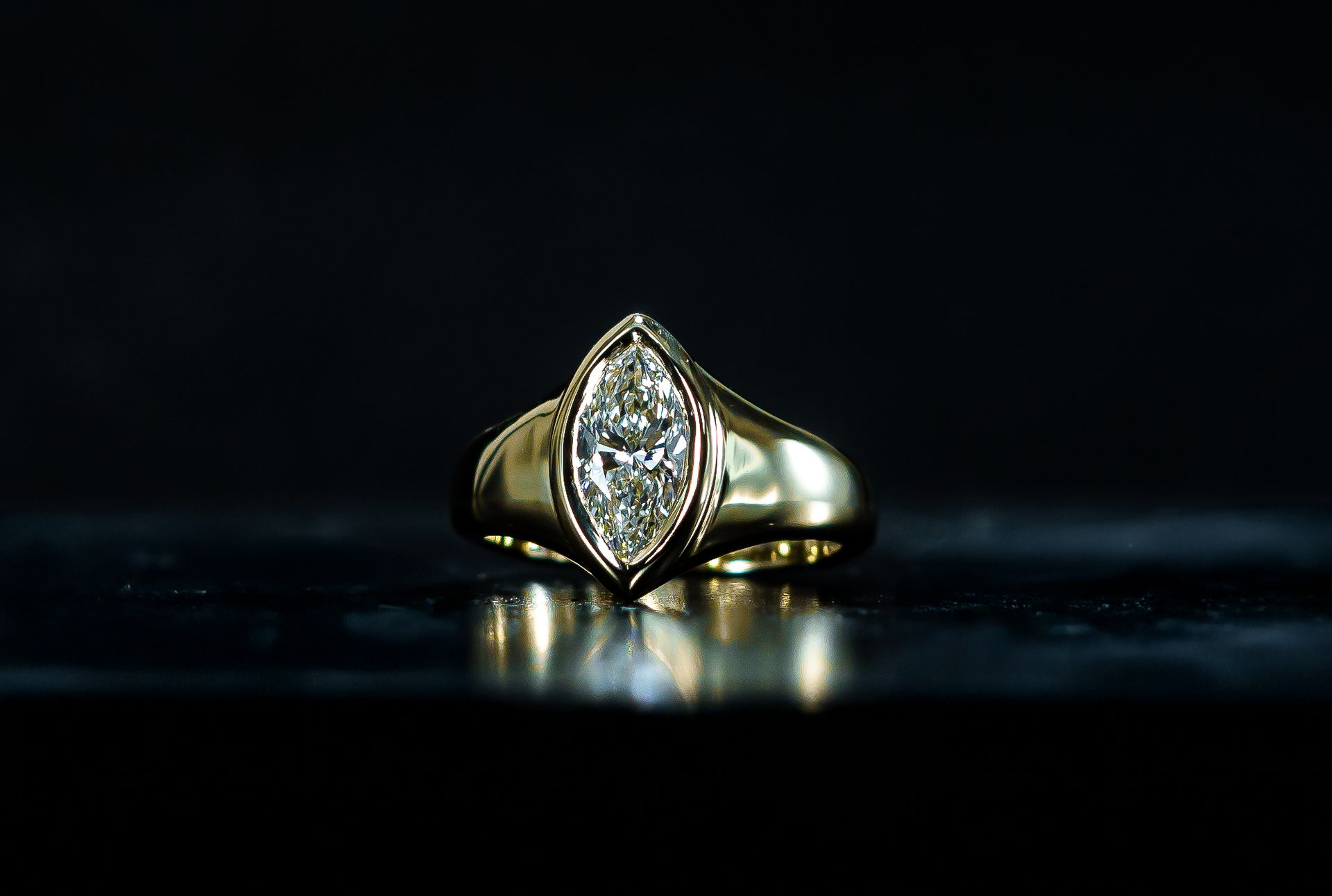 Gold ring with marquise-cut clear gemstone on a dark reflective surface