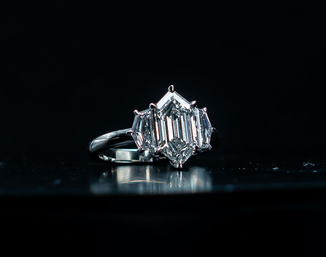 Diamond ring on a dark reflective surface, with a clear rectangular center stone and side stones.