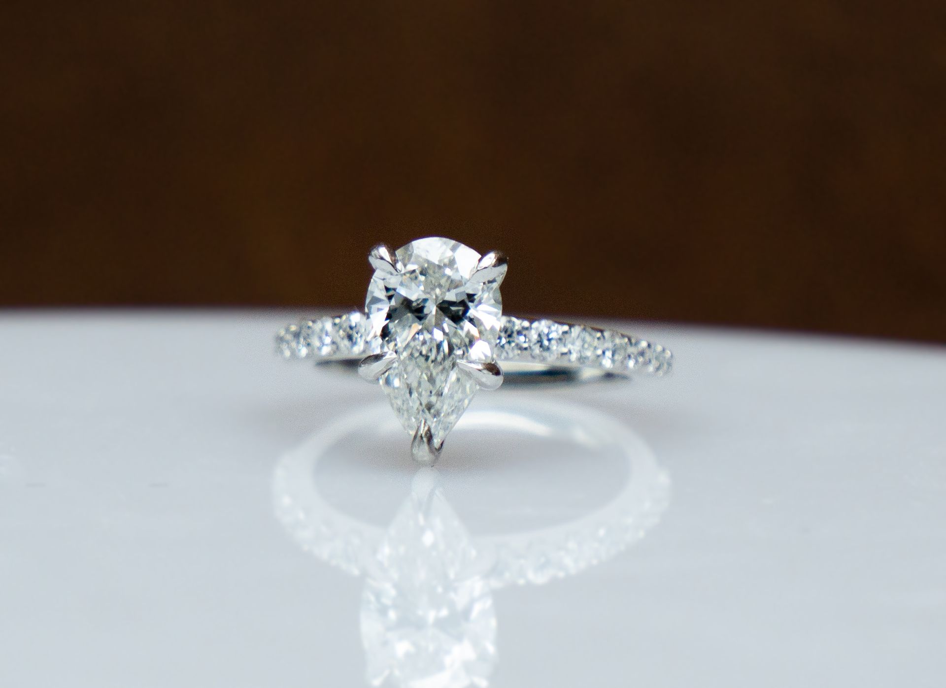 Diamond engagement ring on a white reflective surface against a dark background