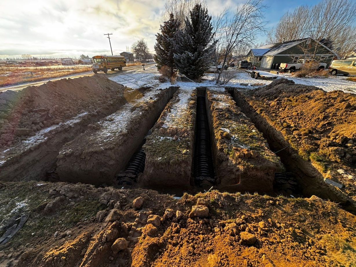 Three deep, parallel trenches cut into a snow-dusted, grassy residential yard with a school bus visible in the distance.