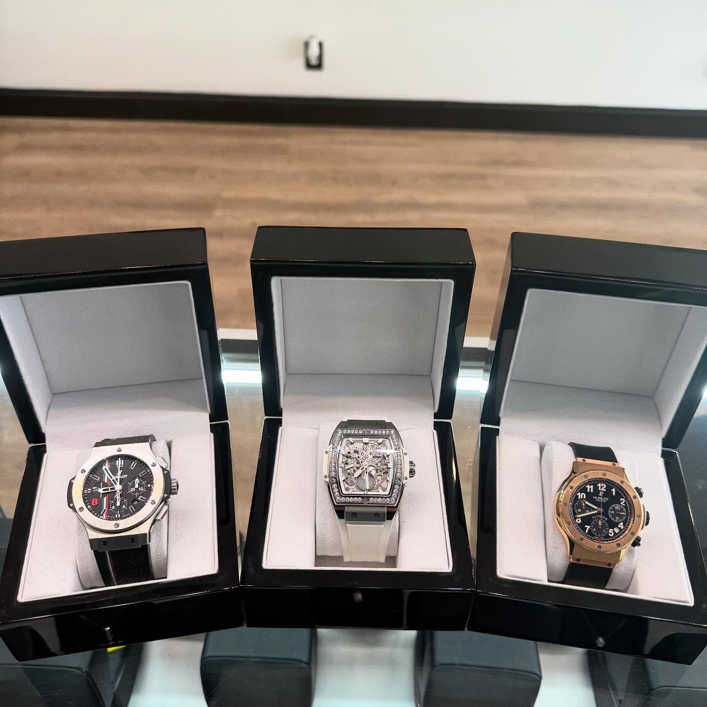 Three wristwatches displayed in black boxes on a table
