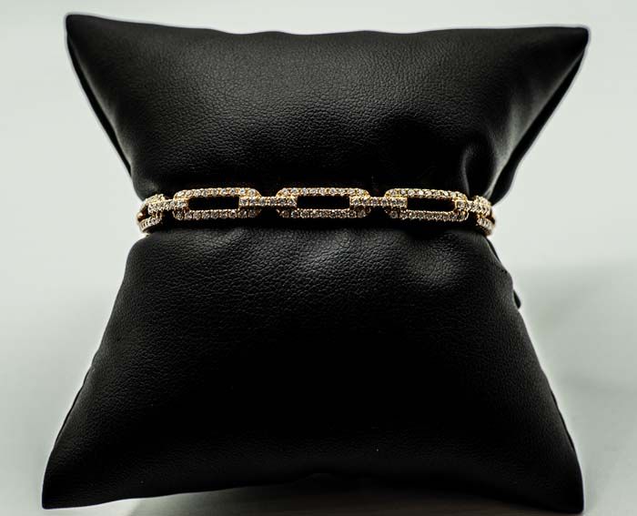 Black leather pillow with a gold chain wrapped around the center on a light background