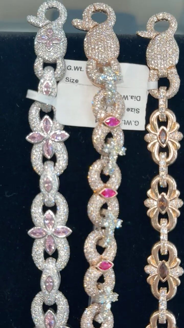 Three sparkly silver bracelets with pink and flower-shaped accents displayed on a black background