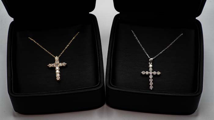 Two silver cross necklaces in black velvet gift boxes, one with clear stones and one with pearl accents