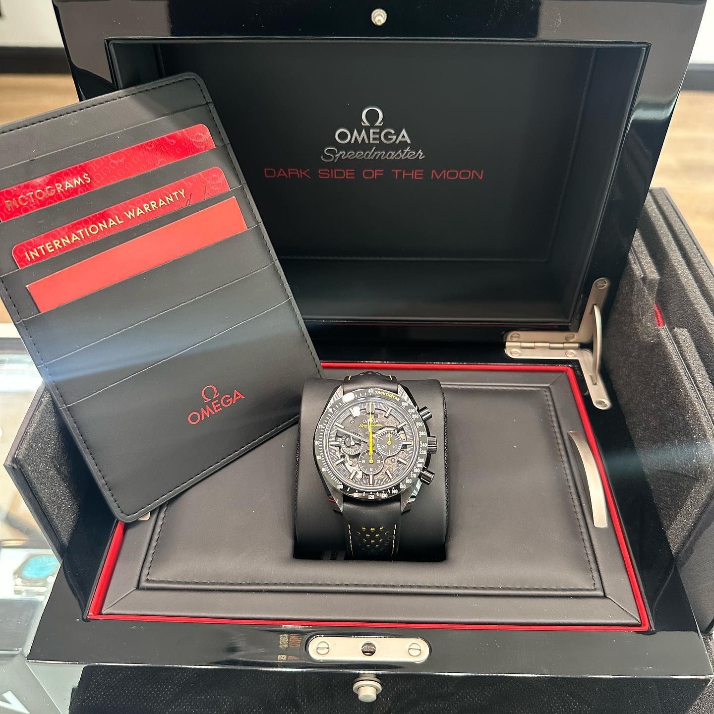Omega watch in an open red-and-black presentation box with warranty cards beside it