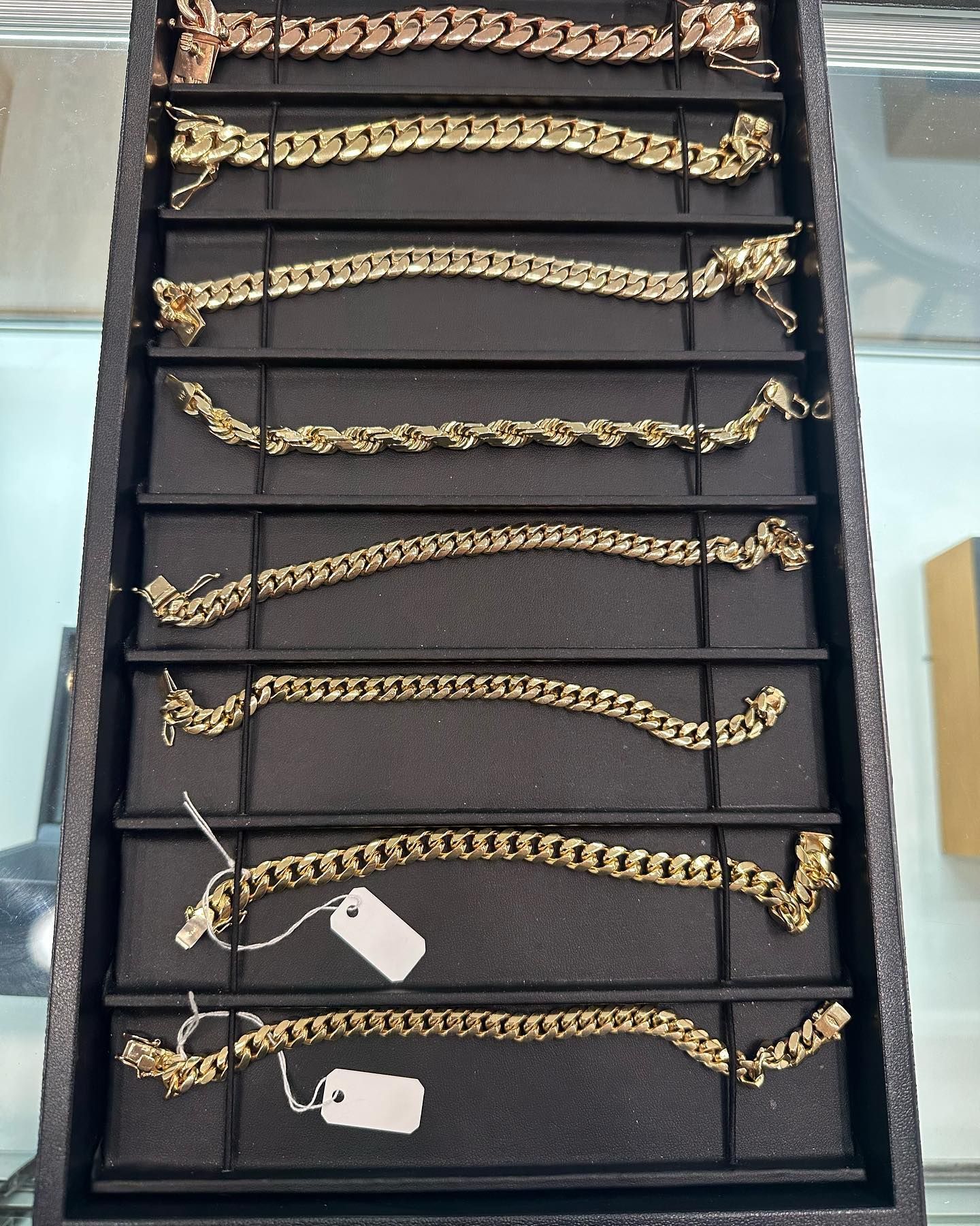 Tray of gold chain bracelets on a black display case in a store.