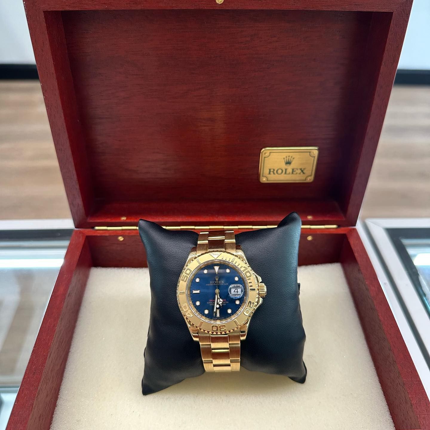 Gold Rolex watch with blue face displayed in an open red presentation box.