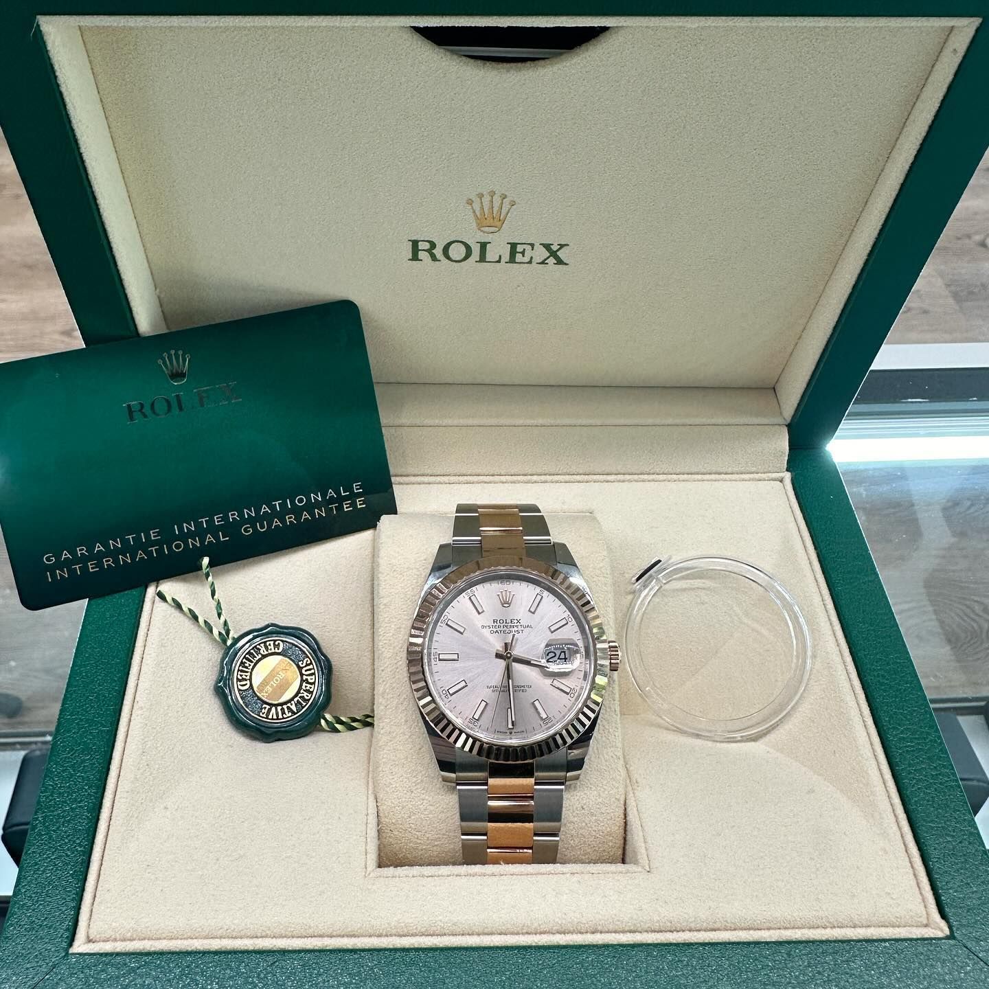 Rolex watch box with two-tone watch, ring, and certificate card inside on a white display tray