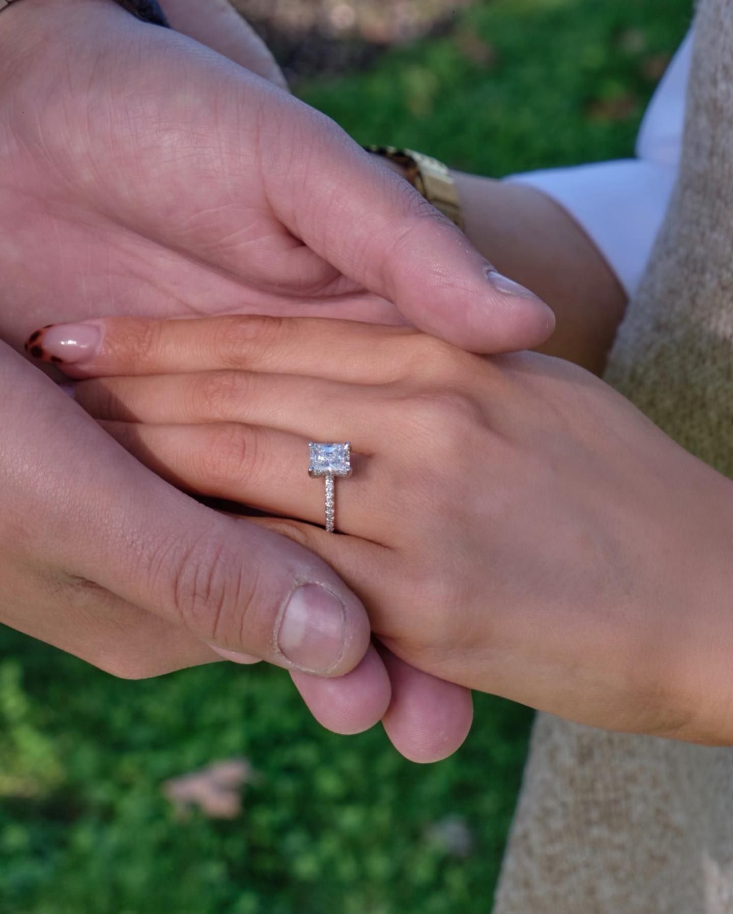 Hands clasped in a proposal, with a diamond engagement ring visible on one finger.