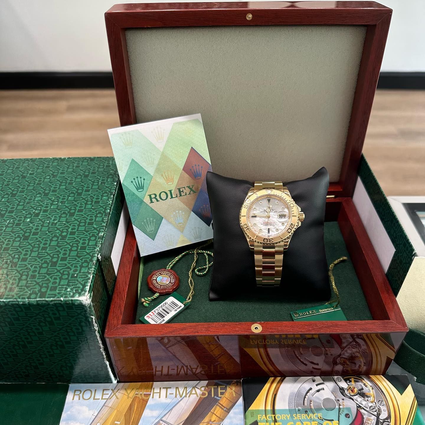 Gold Rolex watch in a presentation box with warranty card and tag on a green surface