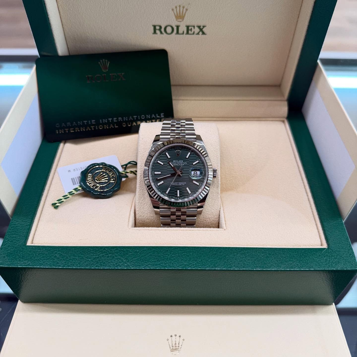Rolex watch in green presentation box with cards and tag on white surface