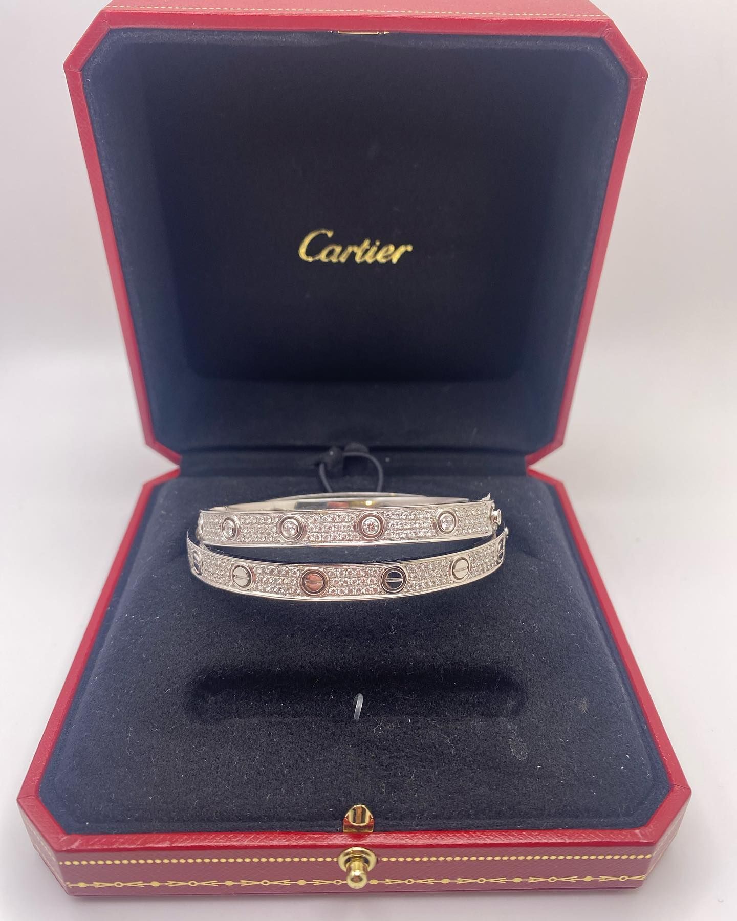 Cartier jewelry box open with two silver bracelets or rings inside on black velvet.
