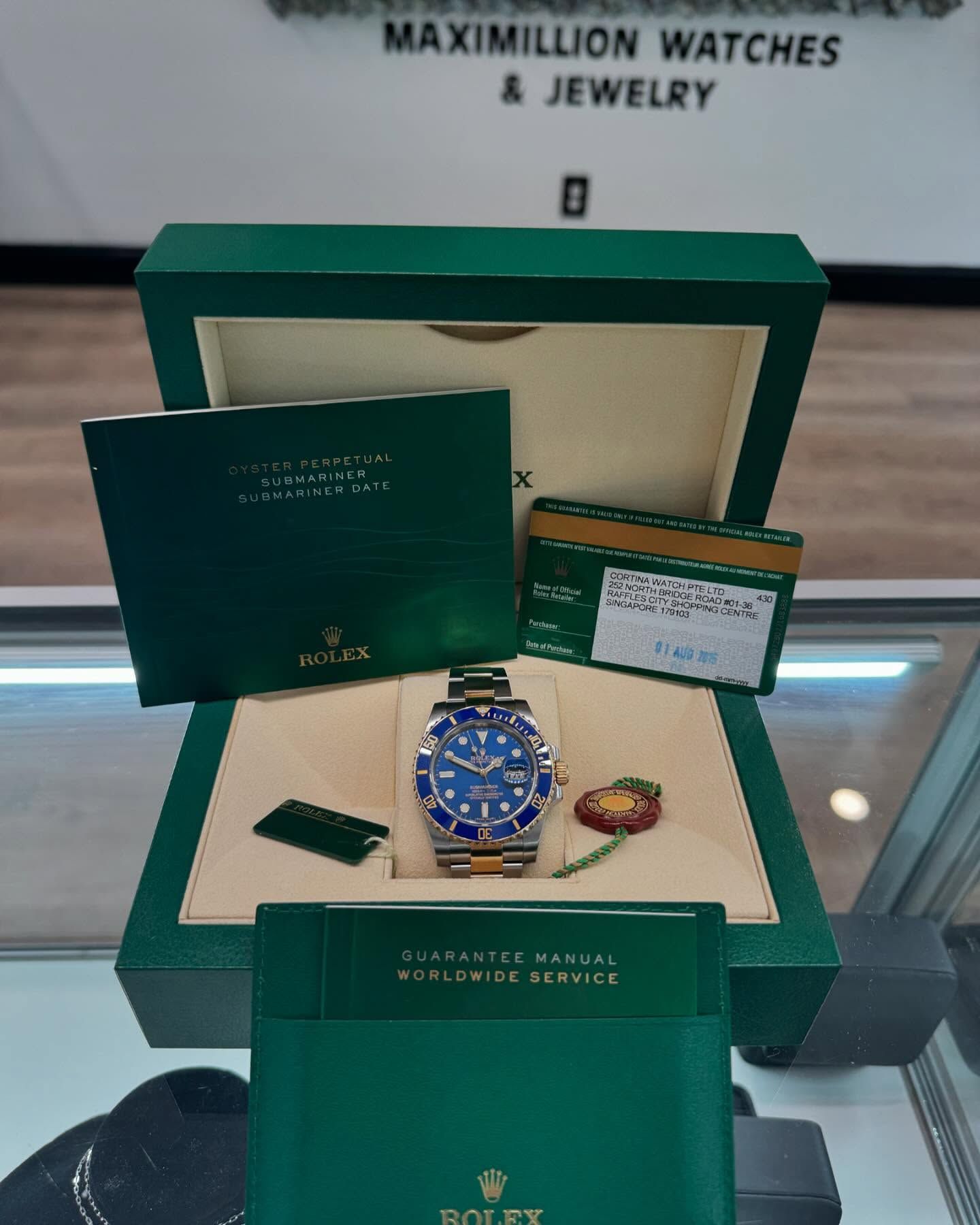 Luxury watch gift box set with a blue Rolex-style watch, green box, and warranty card on display table