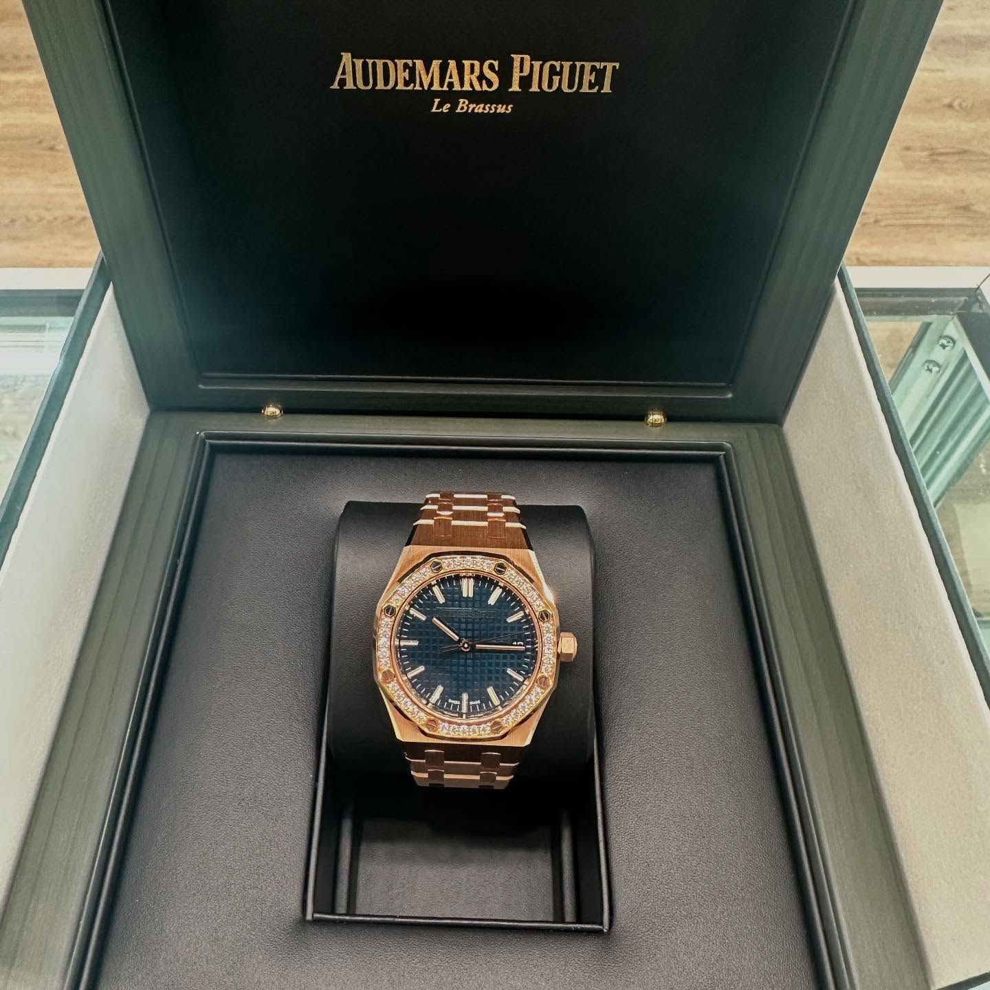 Audemars Piguet rose gold watch in an open presentation box on a glass table.
