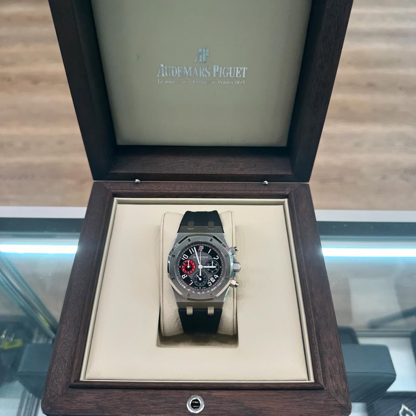 Luxury wristwatch displayed in an open wooden box with beige lining and black strap