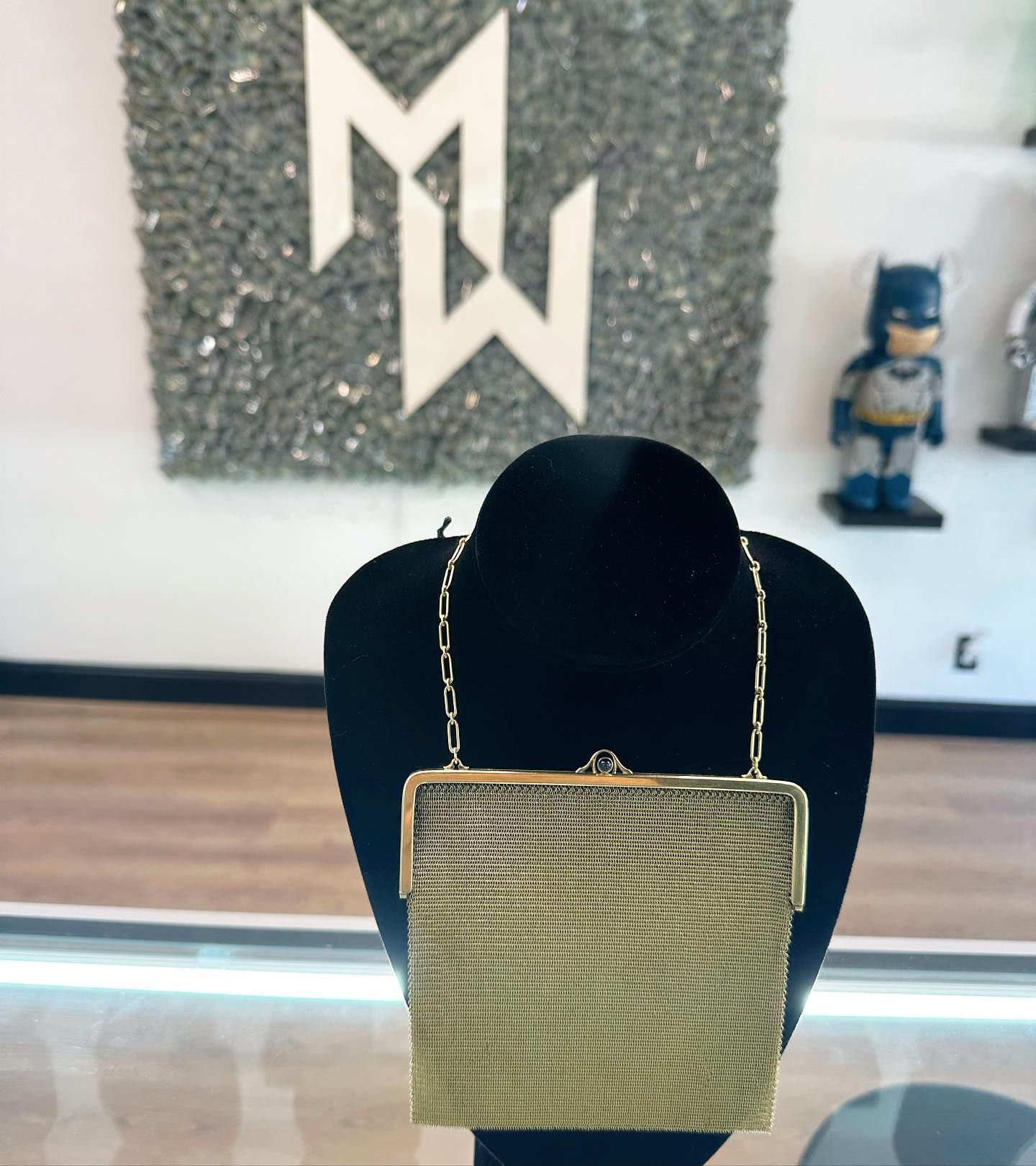 Gold woven square handbag on a black display stand in a store or showroom.