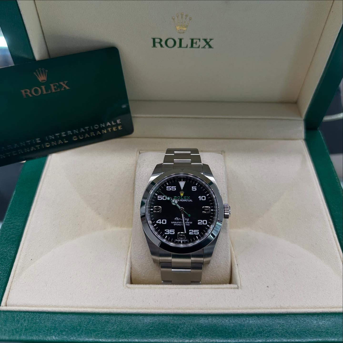 Rolex watch in an open Rolex box with warranty card beside it