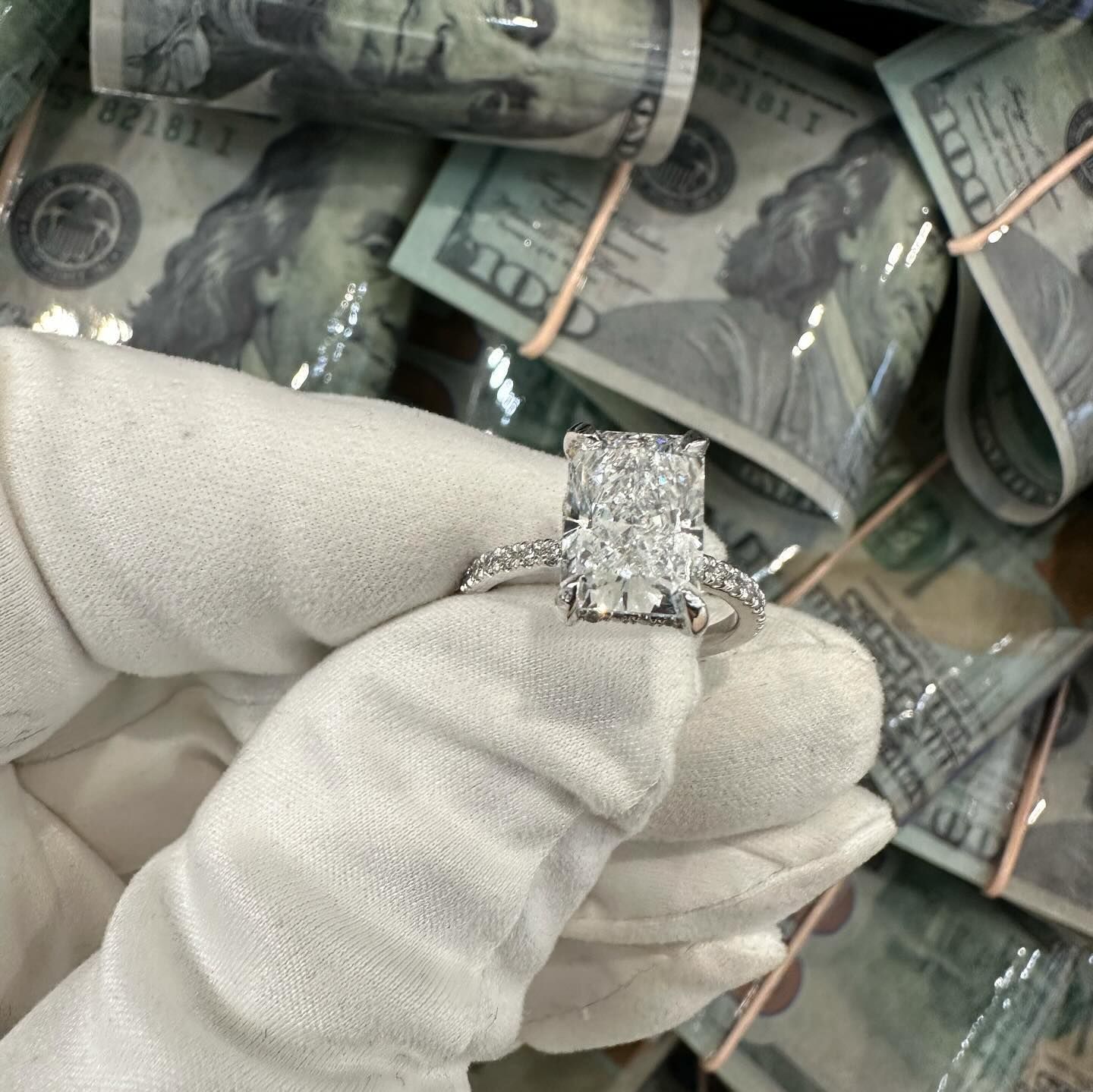 Gloved hand holding a diamond ring in front of stacks of rolled U.S. dollar bills