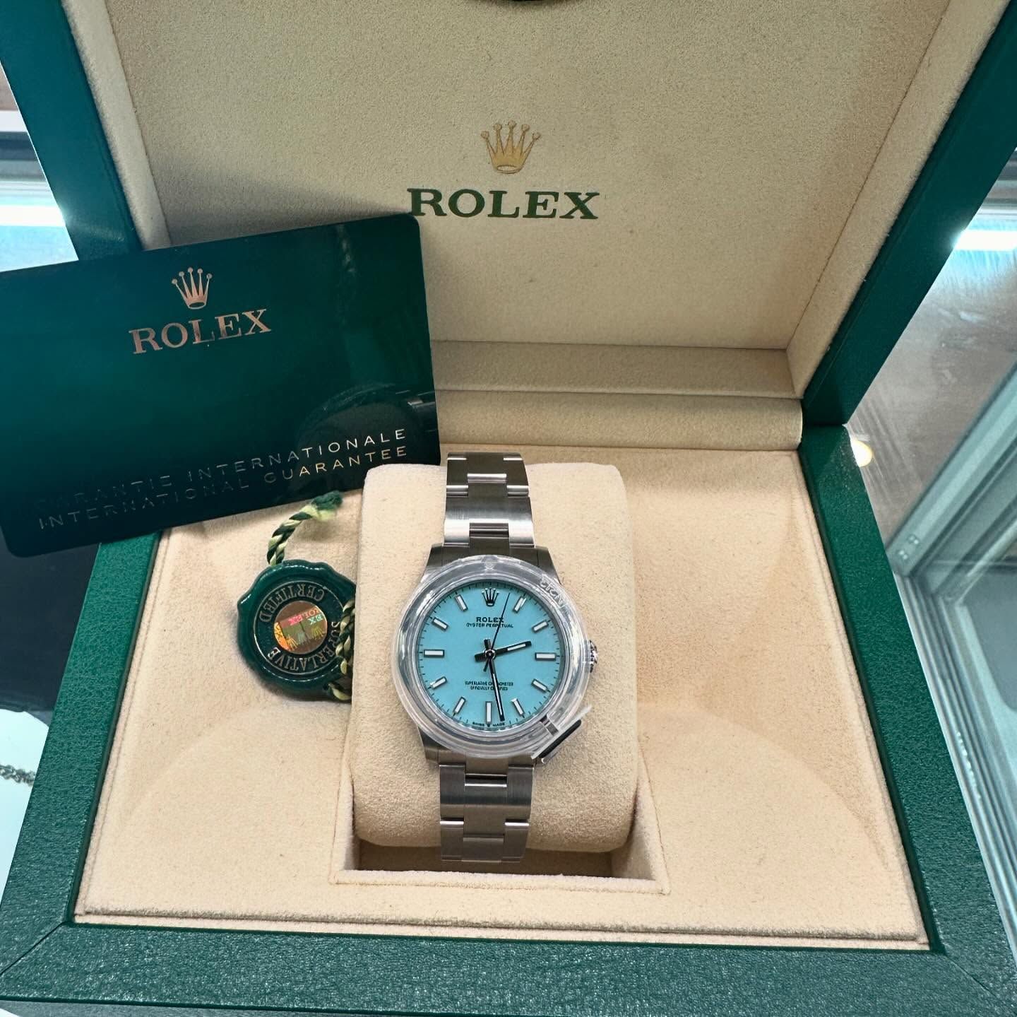 Rolex watch with blue dial in a green presentation box, with a matching hang tag and booklet