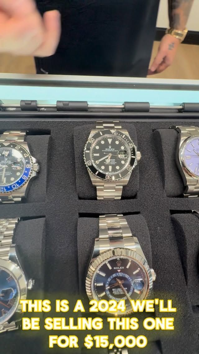 Display of watches in a foam case; a black watch is centered with yellow price text at the bottom.