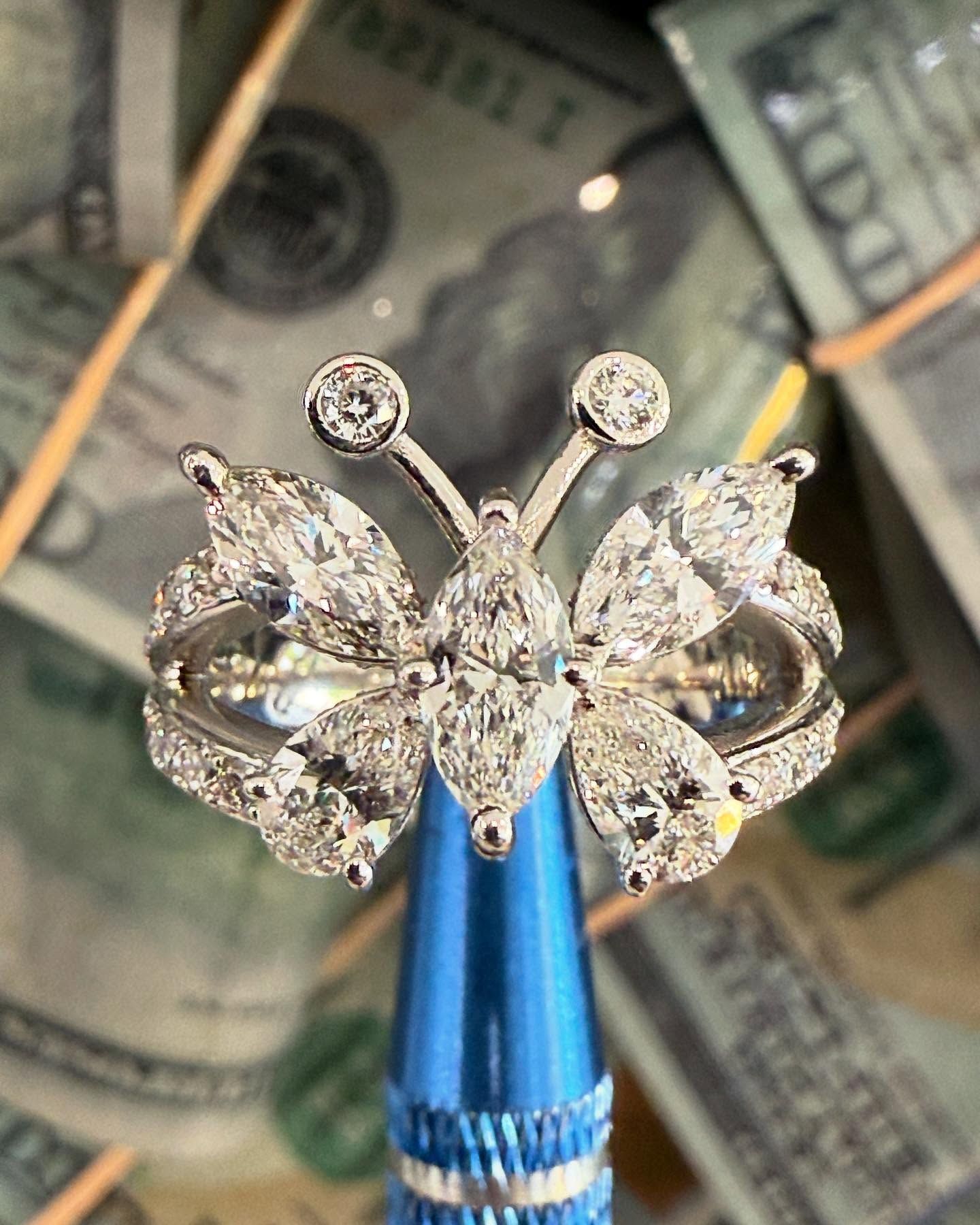 Silver butterfly-shaped ring on a blue holder, with dollar bills blurred in the background