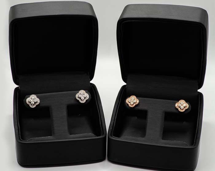 Two open black jewelry boxes displaying matching floral stud earrings, silver on left and rose gold on right.