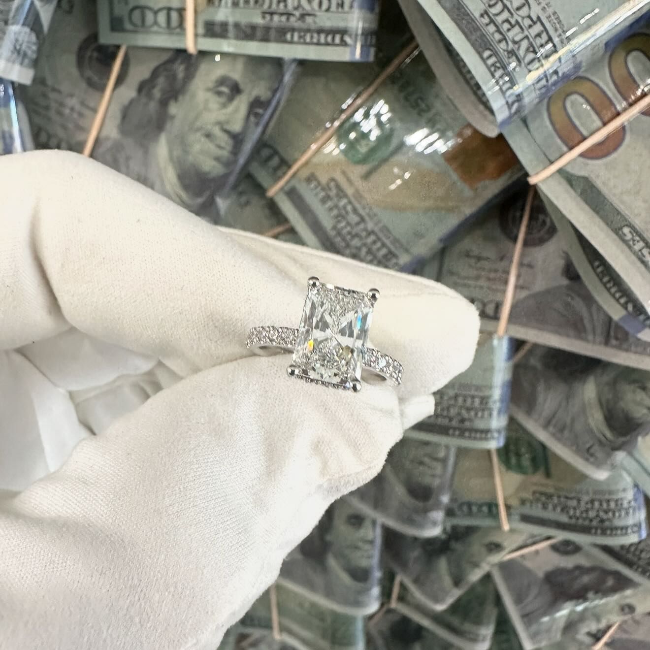 White-gloved hand holding a diamond ring over a background of stacked hundred-dollar bills