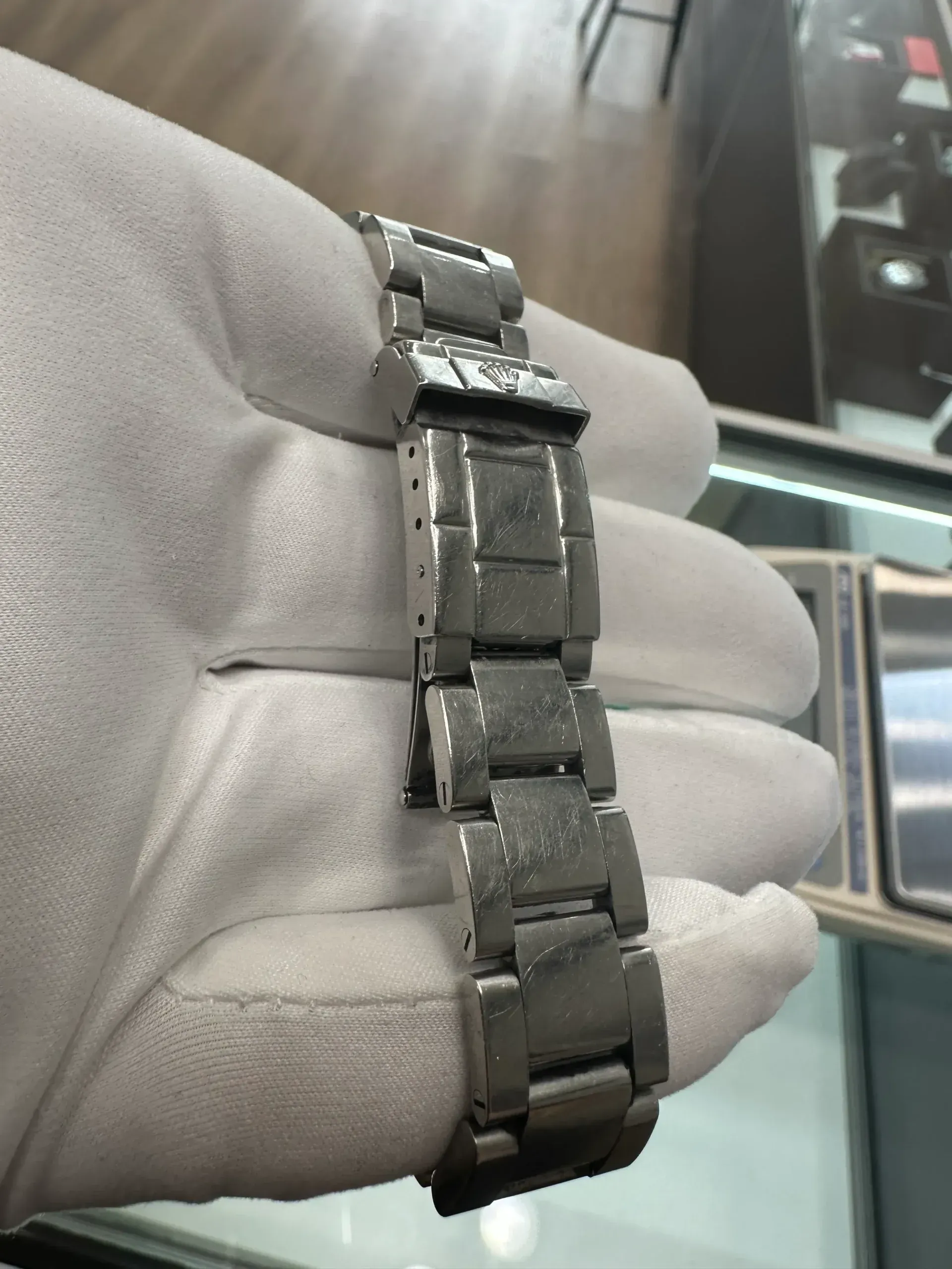 Silver metal watch bracelet held in a gloved hand, shown close-up indoors.