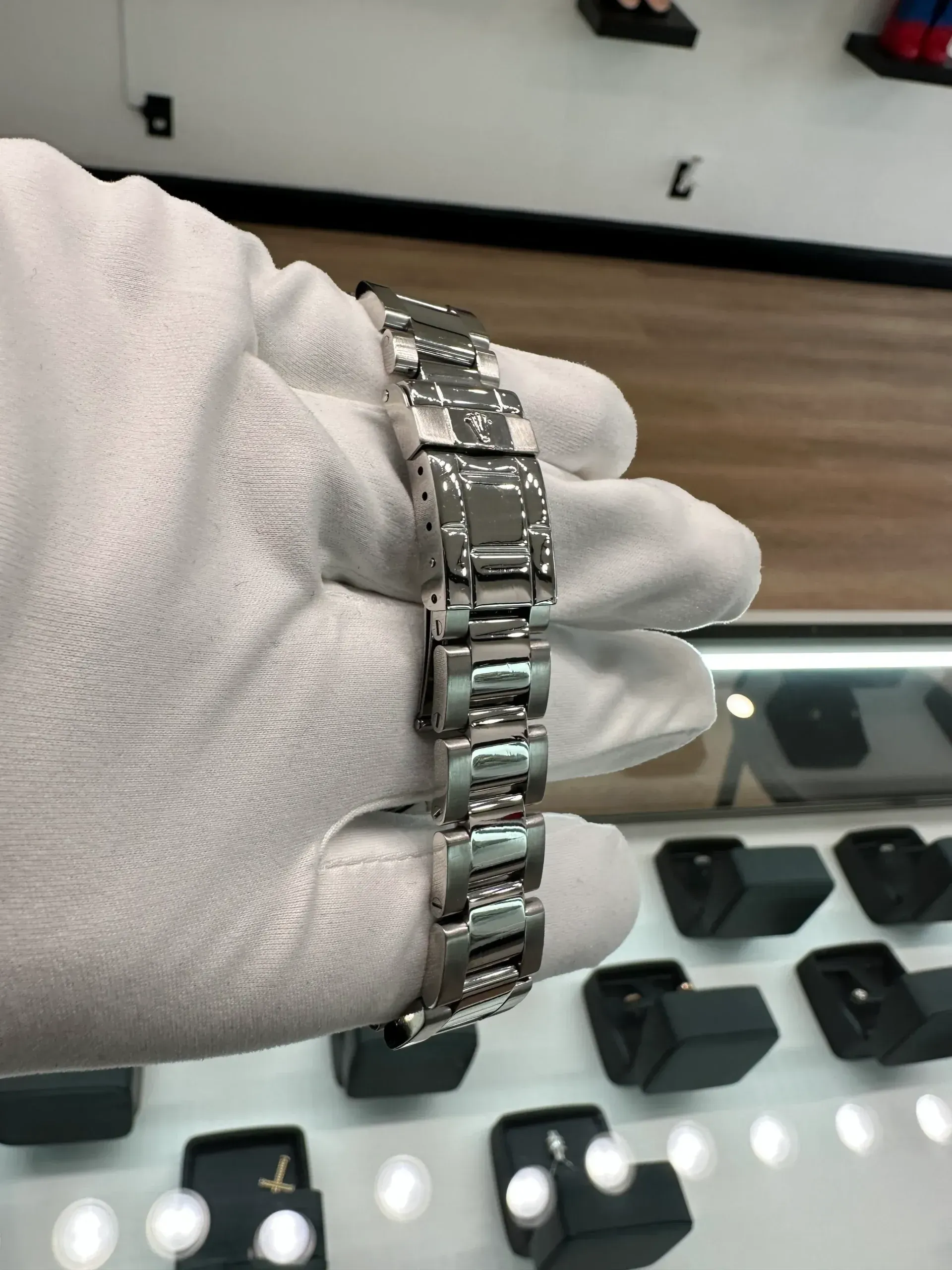 Gloved hand holding a silver bracelet in a jewelry display case